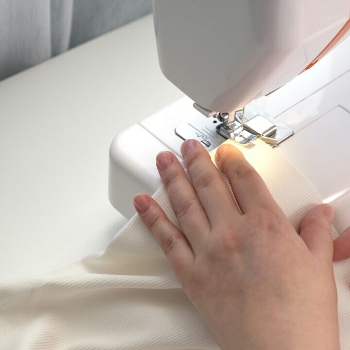 Real middle aged woman tailor sewing clothes using a sewing machine at home. Seamstress working.